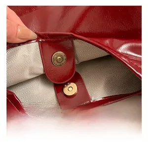 Macro detail of red glossy leather bag featuring magnetic gold clasp and striped lining