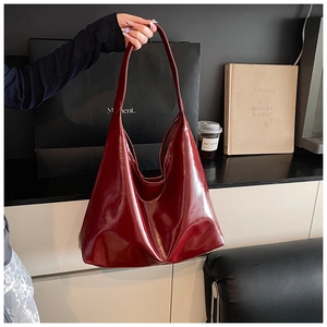 Detail of a burgundy glossy hobo bag with a minimalist slouchy design and wide strap
