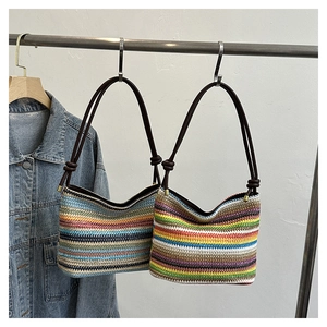 Détail de sacs seaux en paille à rayures colorées avec poignées brunes sur un support