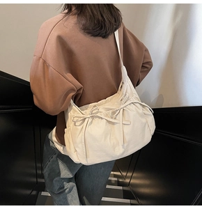 Cream canvas crossbody bag with drawstring bow detail shown on a person's shoulder