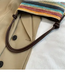 Détail d'un sac seau rayé coloré en paille avec une longue bandoulière en cuir à nœuds
