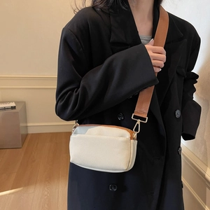 Detail of minimalist canvas crossbody bag with brown leather trim and wide nylon strap