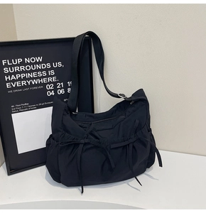 Detail of black nylon crossbody bag featuring drawstring side pockets and decorative bows
