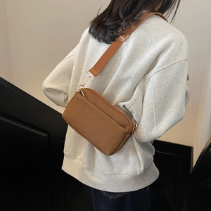 Rear view of model wearing a brown canvas crossbody bag with adjustable strap and zipper details