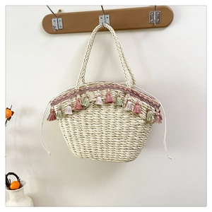 Detail of a cream woven straw bag featuring colorful tassel trim and braided handles