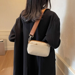 Detail of beige canvas crossbody bag with a wide brown strap worn over a black blazer