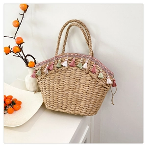 Detail of hand-woven straw tote bag with multi-colored tassels and woven ring handles