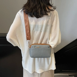 Detail of grey canvas crossbody bag with wide brown strap worn by a model from the back