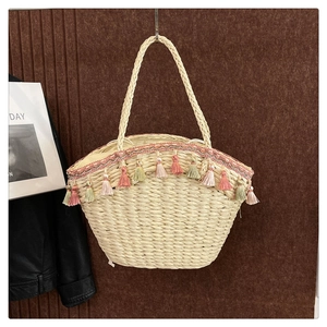 Detailed close-up of straw beach bag with pink tassels and embroidery hanging on a wall