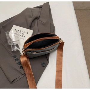 Detail view of a multi-layer mini crossbody bag with three golden zipper compartments