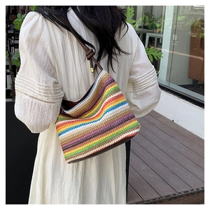 Sac seau en paille à rayures colorées avec bandoulière en cuir sur une robe blanche