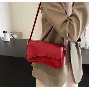 Détail du sac à bandoulière rouge en similicuir brillant avec rabat ondulé et texte doré