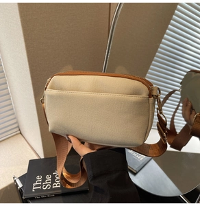Detail of off-white canvas crossbody bag with brown zippers and wide nylon strap