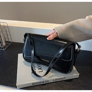 Détail d'un sac d'épaule en cuir verni noir avec inscription FASHION & BAGS et fini brillant