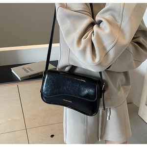 Détail du sac à épaule en similicuir noir avec logo doré et texture légèrement froissée