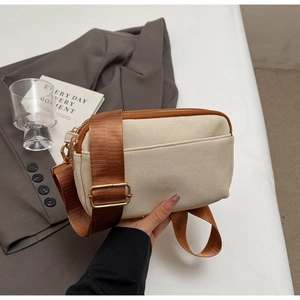Detail of beige canvas crossbody bag with dual zippers and brown adjustable strap
