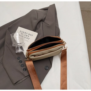 Detail of a two-tone crossbody bag featuring dual zippers and a wide fabric shoulder strap