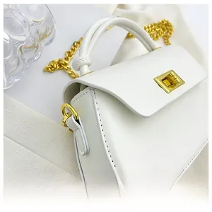 Detail of white leather mini crossbody bag featuring a gold twist lock and knotted handle