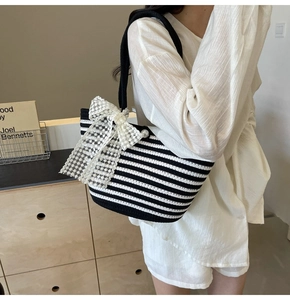 Detail of striped woven beach bag featuring a lace bow and large pearl clasp detail