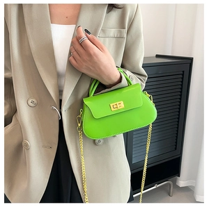 Detail of neon green chain bag with gold metal lock and handle worn on khaki blazer