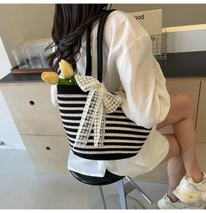 Close-up of a striped woven tote bag with a white lace bow detail and slim black straps