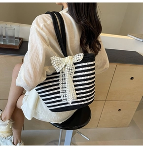 Detail of striped woven tote bag featuring a white lace bow accent for casual holiday style