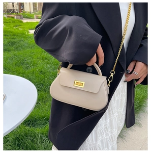 Detail of a creamy leather mini square bag with golden chain and clasp on a model