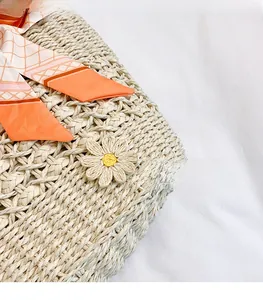 Dettaglio borsa intrecciata beige con ciondolo a margherita e foulard in seta arancione