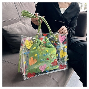 Detail of transparent PVC tote bag with colorful heart prints and green drawstring inner bag
