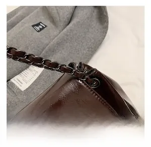 Close-up of glossy oil wax leather shoulder bag with polished gunmetal chain strap detail