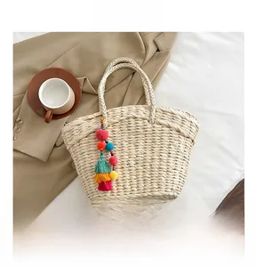 Detail of woven straw handbag with colorful tassels showing size next to a smartphone