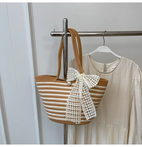 Detail of striped woven beach bag with lace bow and pearl accent hanging on a rack