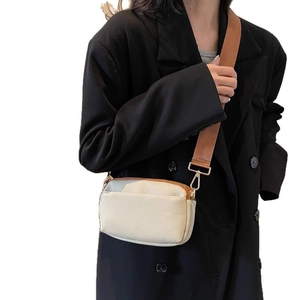 Minimalist beige crossbody camera bag with brown wide strap worn over a black blazer