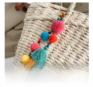 Macro detail of colorful pompom tassel charm with wood beads on woven straw bag