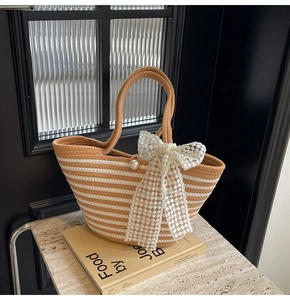 Detail of striped woven tote bag featuring a pearl clasp and large white lace bow accent