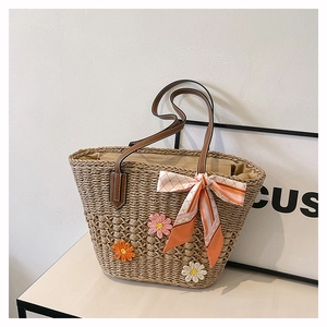 Dettaglio borsa in paglia intrecciata con fiori all'uncinetto e fiocco di seta a quadri