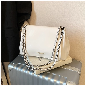 Close-up of white leather chain bag with gold embossed text on a silver suitcase