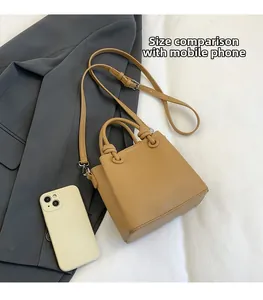 Mini khaki pebble leather handbag with adjustable strap shown next to a smartphone