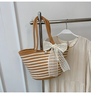 Detail of striped straw tote bag featuring a large lace bow and elegant pearl accent