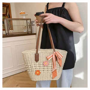 Dettaglio borsa shopper in paglia con foulard in seta, manici in pelle e fiori in maglia