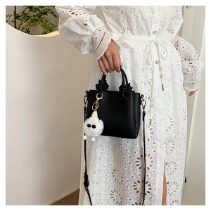 Detail of black pebbled leather handbag with knot handles and plush charm on white lace dress