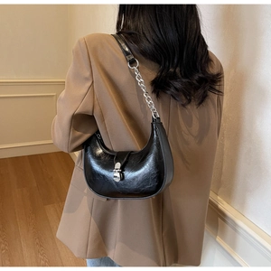 Gros plan d'un sac demi-lune noir brillant avec chaîne argentée et boucle en métal