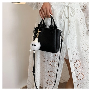 Chic black pebble leather handbag with knot handle and plush charm on white lace dress