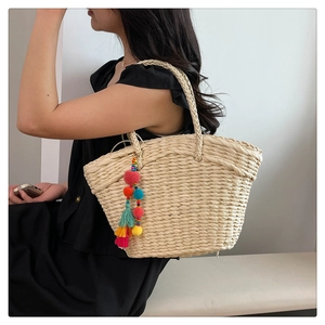 Straw tote bag with colorful pompom tassel and drawstring lining shown from the side