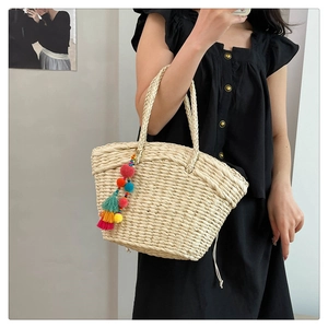 Detail of hand-woven straw tote bag with colorful pompom tassel charm on the handle