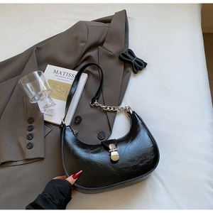 Détail du sac hobo noir brillant avec boucle argentée et chaîne sur blazer marron
