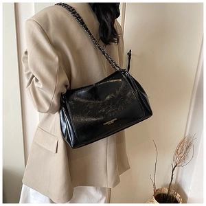 Detail of a black glossy leather crossbody bag with metallic chain and gold lettering