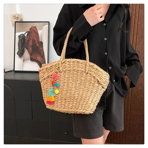 Close-up of woven straw tote bag featuring colorful pom-poms and tassel charms