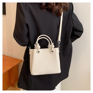 Close-up of beige leather handbag featuring textured lychee grain and knot handle detail