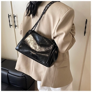 Close-up of black glossy leather chain bag with gold logo on beige suit background